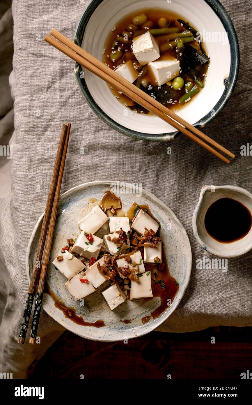 Zuppa giapponese di brodo miso con cubetti di tofu di seta, edamame di fagioli di soia, fagioli verdi in ciotola tradizionale, tofu condimento speziato con bacchette su lino grigio ta Foto Stock