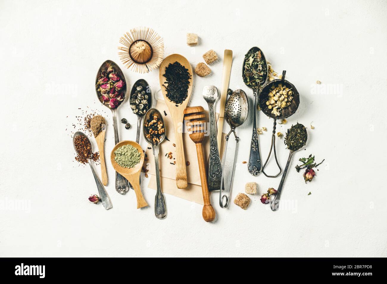 Composizione creativa con vari tipi di tè secco, cucchiai di argento e bambù e zucchero su sfondo bianco tela di wintage, posa piatta, vista dall'alto Foto Stock