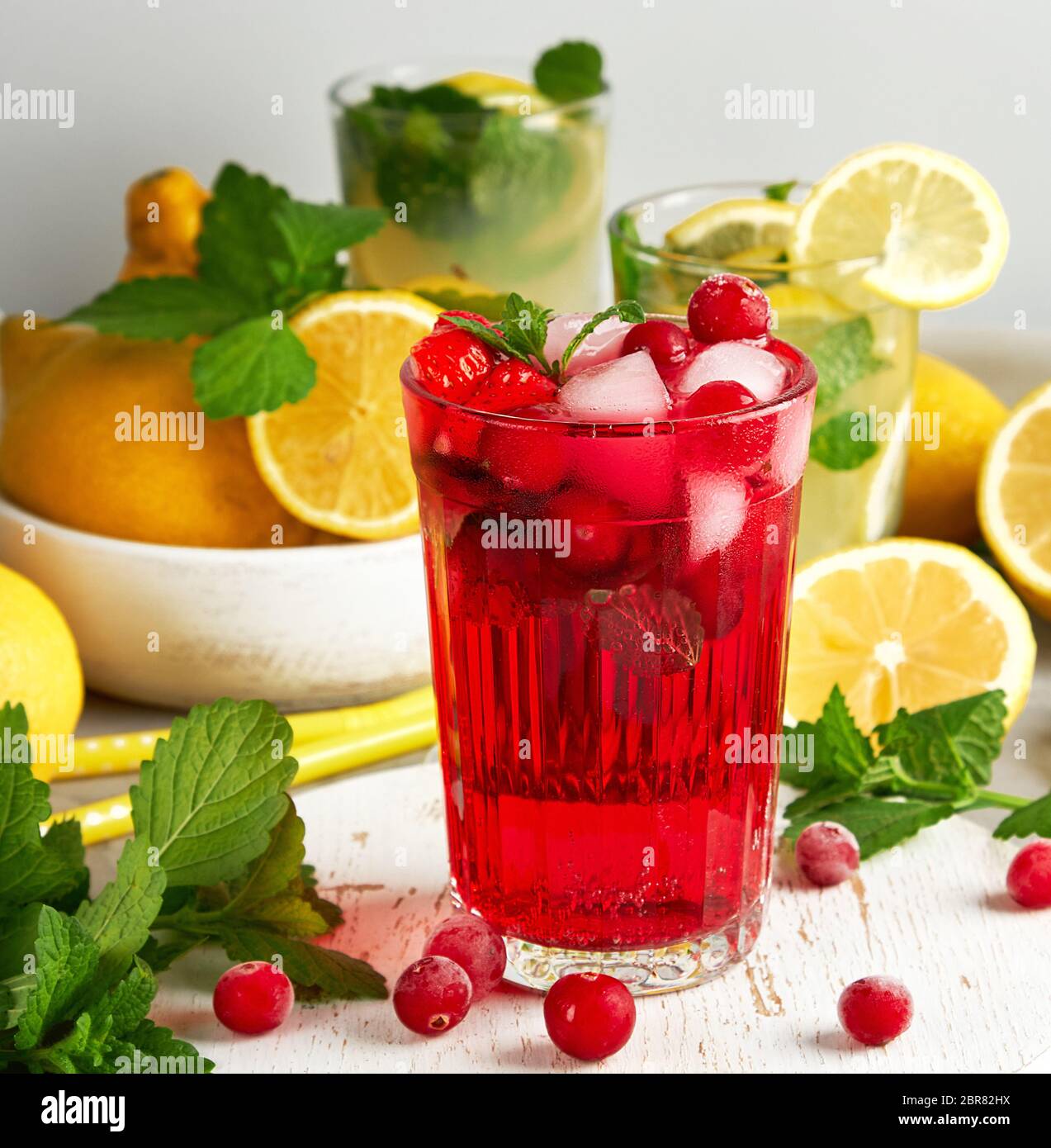 Dissetante bevanda estiva di fragole e mirtilli rossi su un bianco tavola di legno, dietro di esso sono il giallo dei limoni e il verde di foglie di menta Foto Stock