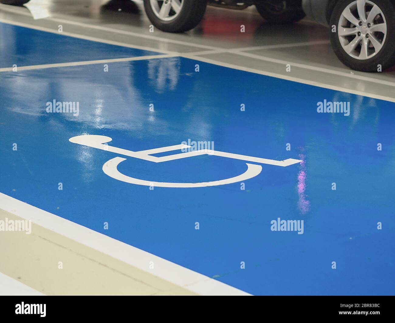 Posto auto per disabili in garage, area blu luminosa con il simbolo dipinto di bianco di una sedia a rotelle, sul bordo superiore riconoscibile per il siero Foto Stock