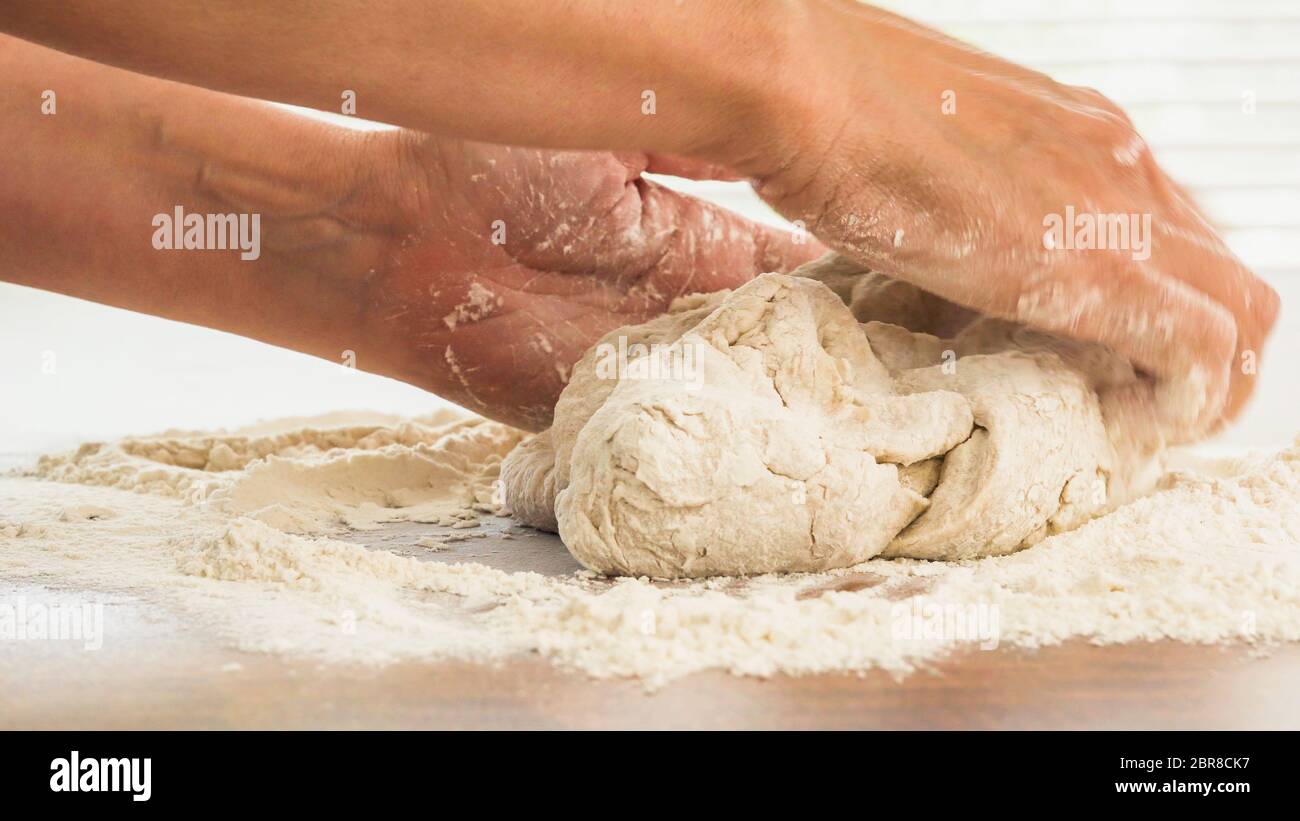 Impasto di pane o pasta per pizza da vicino su tavolo da cucina in legno. Mani di donna impastando l'impasto di pane di farina integrale Foto Stock