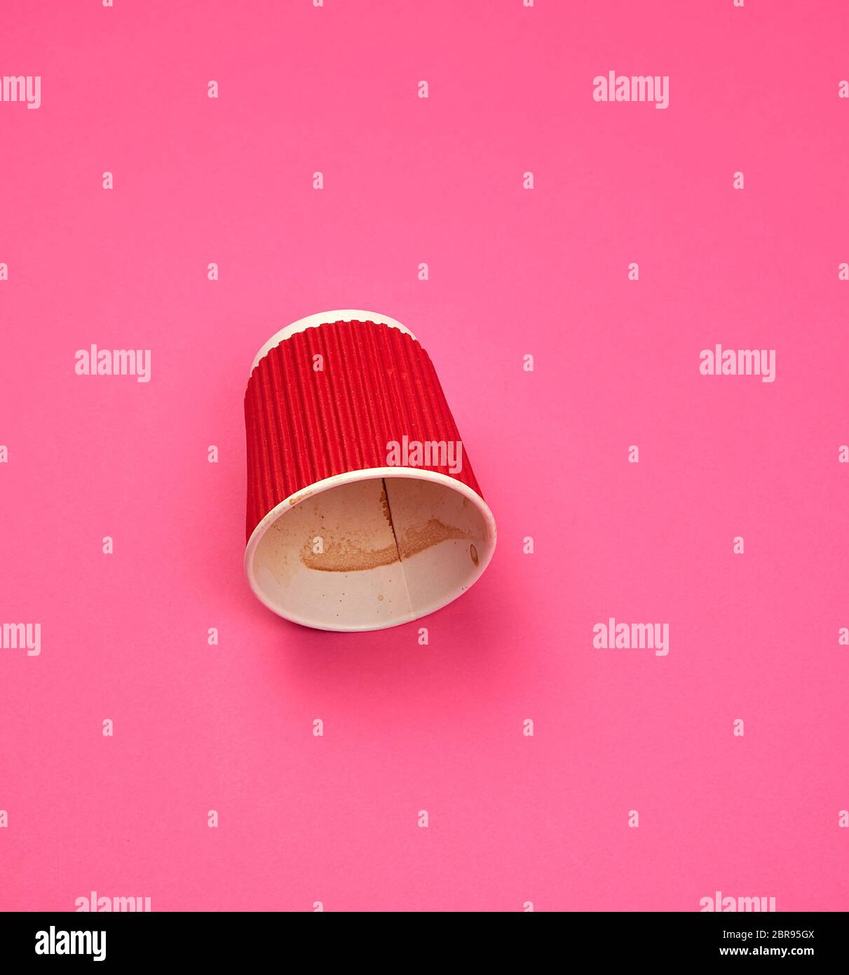 Utilizzate la carta red cup con bordi ondulati dal caffè capovolto su un sfondo rosa Foto Stock