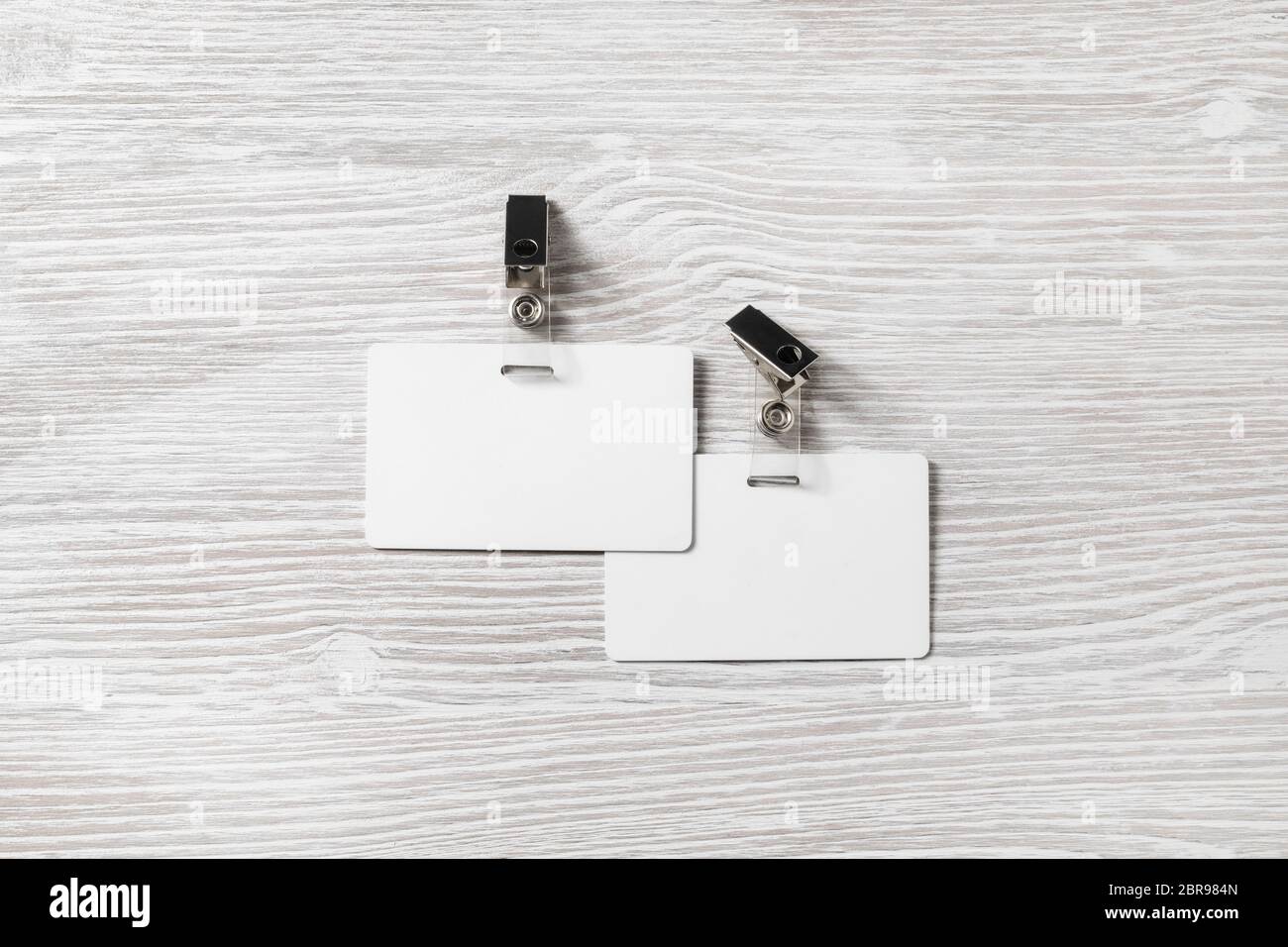 Foto di due vuoti in plastica bianco scudetti mockup sulla luce sullo sfondo di legno. Le schede Id mock up. Spazio per il testo. Lay piatto. Foto Stock