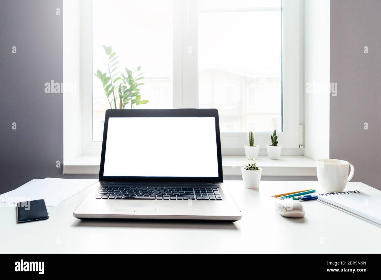 Luogo di lavoro con computer portatile con schermo vuoto su tavolo bianco con mouse e tazza di caffè. Ufficio domestico e lavoro remoto. Foto Stock