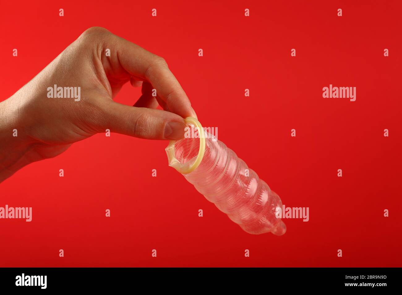 Close up man mano che tiene una aperta del condom in lattice su sfondo rosso con copia spazio, basso angolo vista laterale Foto Stock