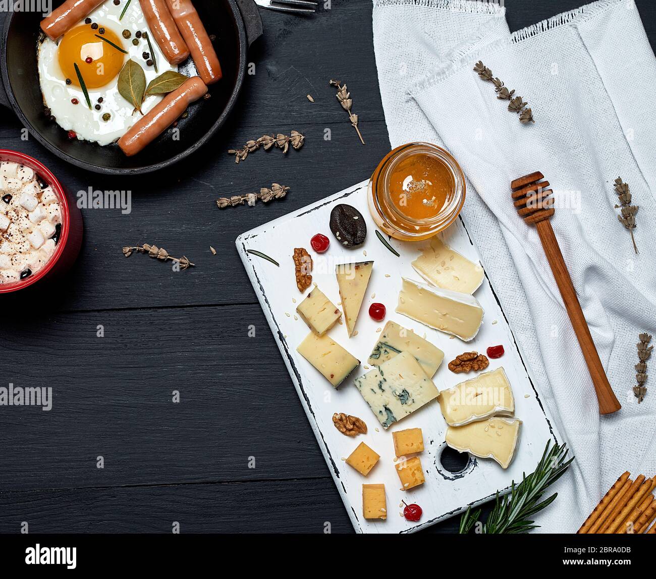 Uovo fritto con salsicce in un tondo nero padella con una maniglia, una scheda con diverse fette di formaggio e una tazza di caffè e la colazione per uno, parte superiore vi Foto Stock