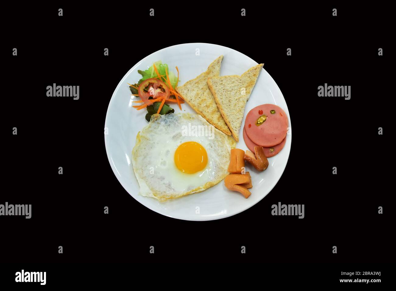 colazione su piatto bianco, uova fritte, pane, prosciutto, salsiccia e qualche vegetale.top vista image.saved clipping path.isolato sfondo nero. Foto Stock