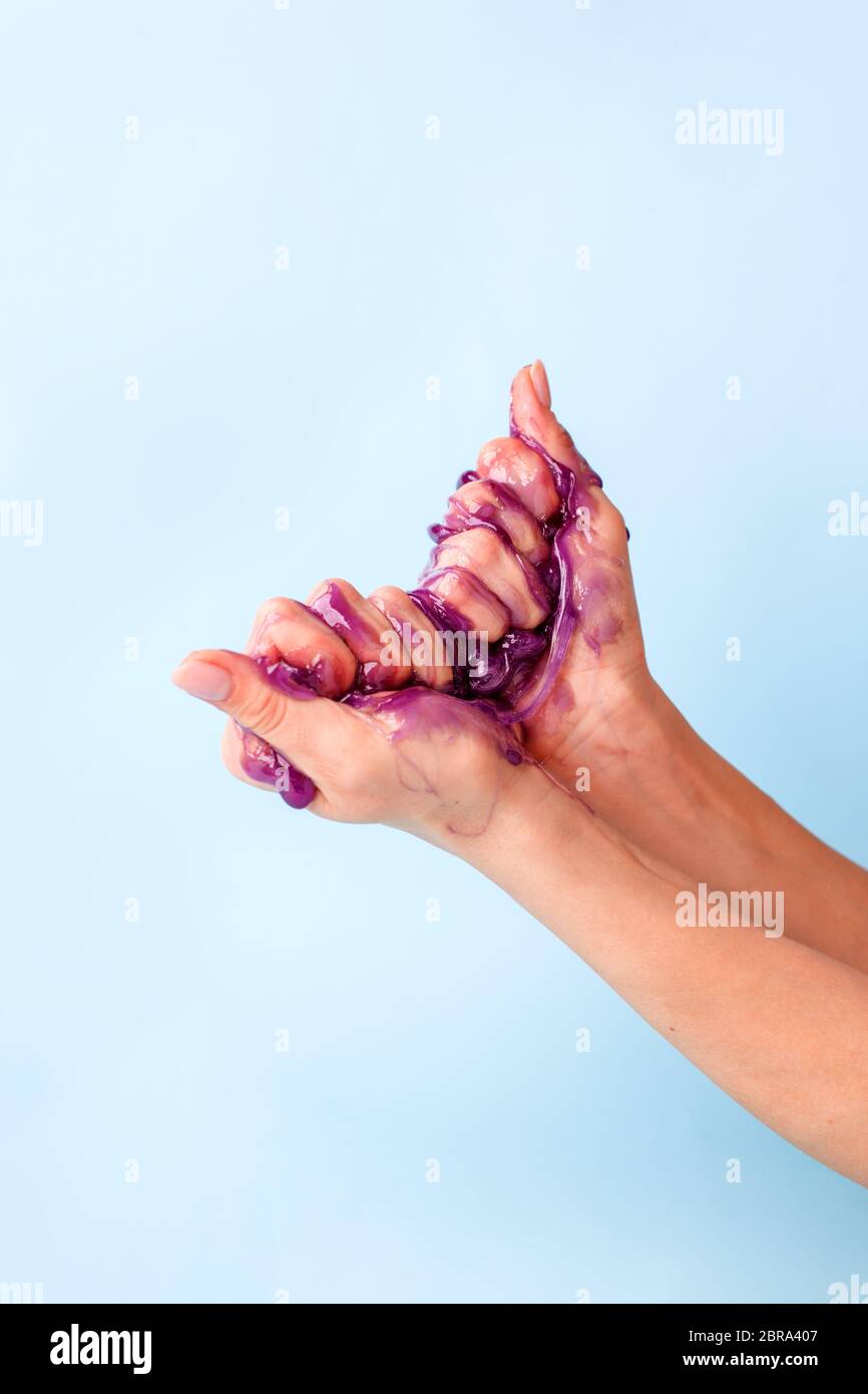 Mani di giovane ragazza con melma viola appiccicosa su sfondo blu, cera liquida per depilazione, banner concettuale con spazio di copia, antistress relax, mo Foto Stock