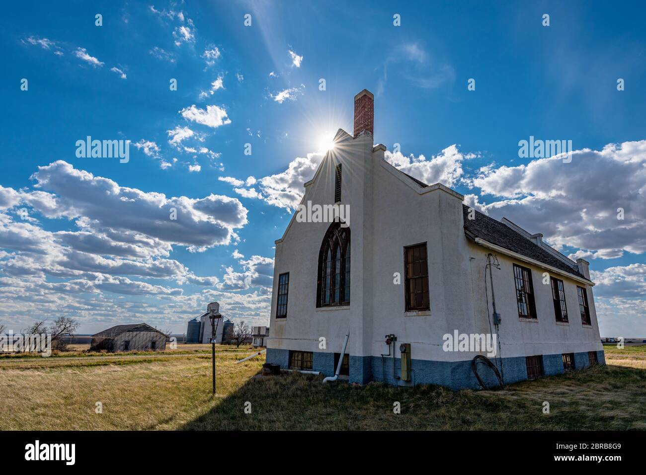 Sunburst sopra la chiesa unita abbandonata di Lacadena e elevatore di grano a Lacadena, Saskatchewan, Canada Foto Stock
