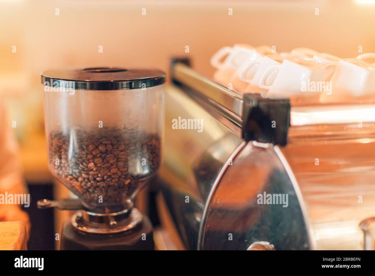 Chicchi di caffè nel macinacaffè con tazze bianche. Sfondo artistico della caffetteria Foto Stock