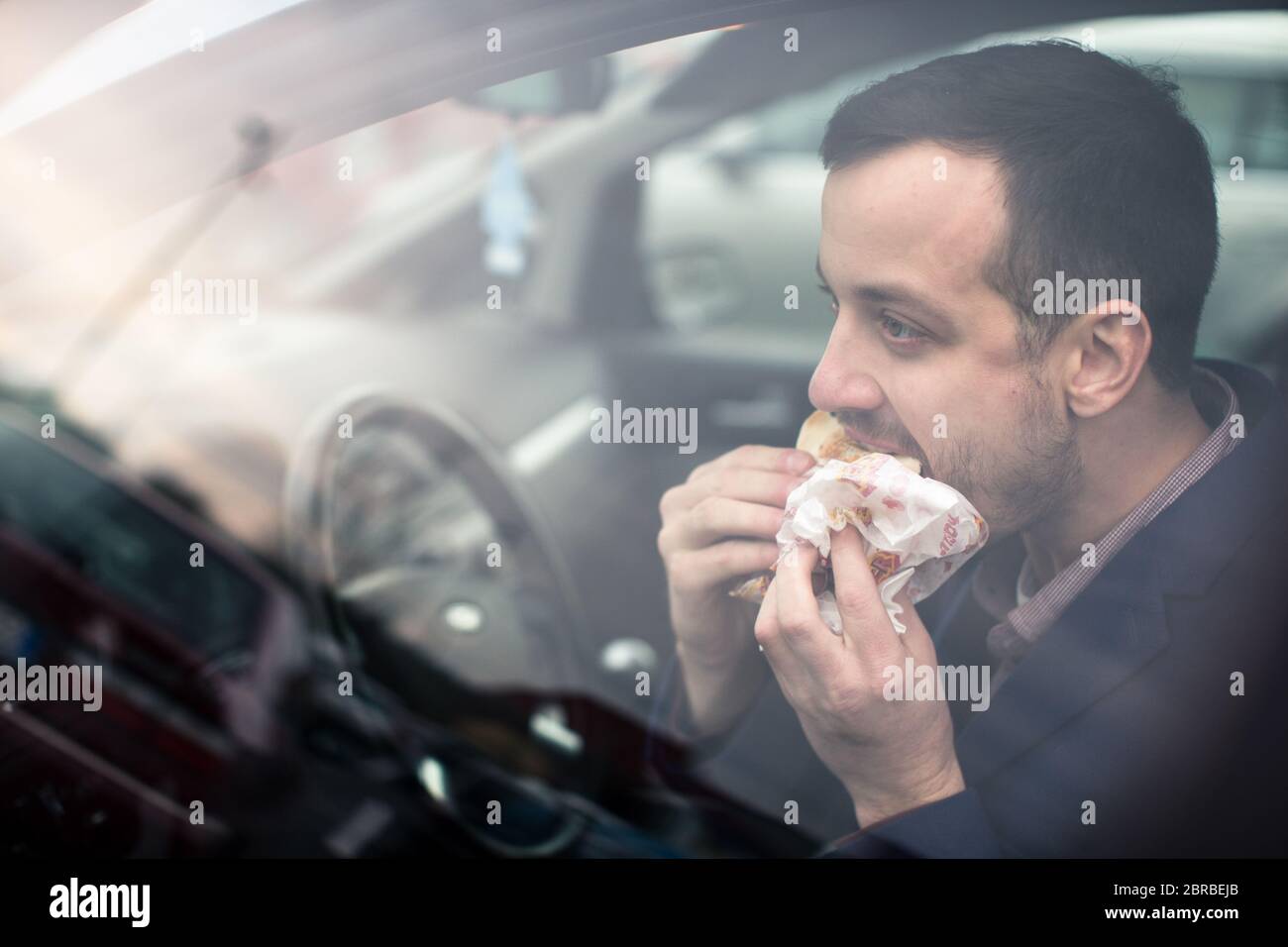 Bel giovane mangiare un frettoloso pranzo nella sua auto (toni di colore immagine; shallow DOF) Foto Stock