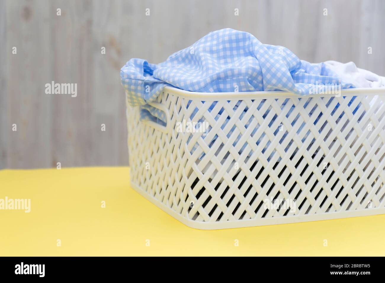 Camicie bianche blu in un cestello di plastica bianca su un tavolo giallo su sfondo grigio. Lavanderia, pulizia della casa, pulizia e freschezza Foto Stock