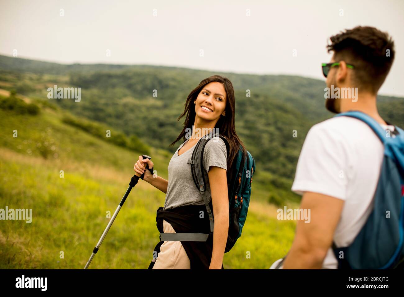 Giovane coppia sorridente che cammina con zaini su verdi colline Foto Stock