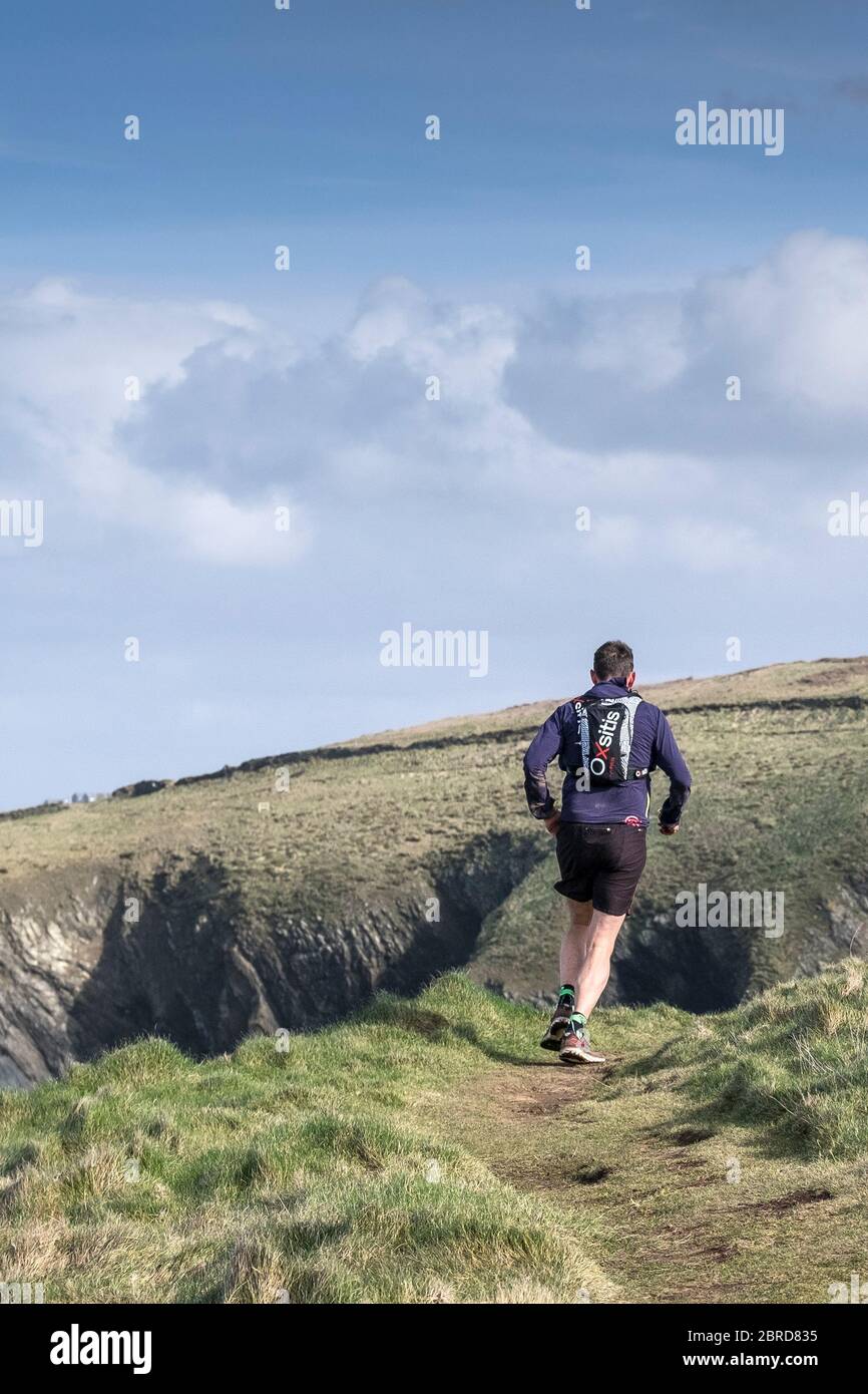 Un uomo che corre su un sentiero lungo il Penth Point East sulla costa di Newquay in Cornovaglia. Foto Stock