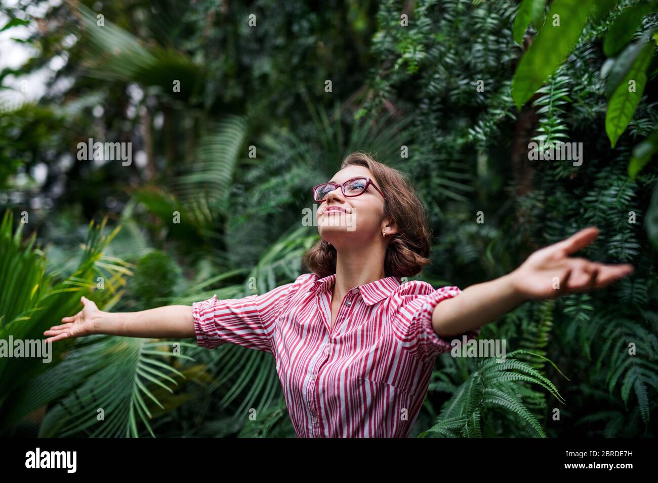 Giovane donna in piedi in giardino botanico, braccia tese. Foto Stock