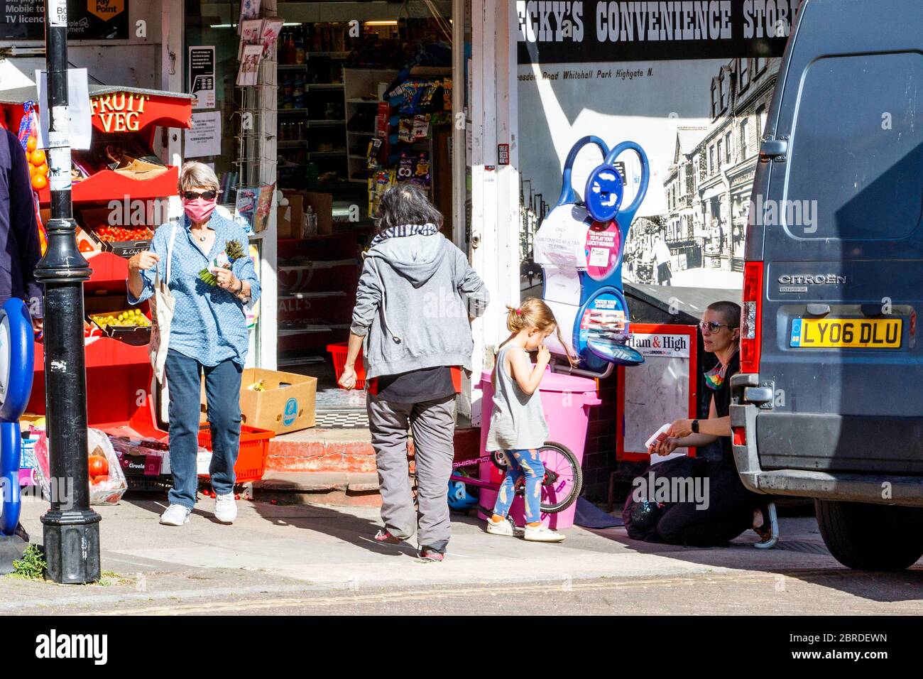 Londra 19 2020 maggio quando il bilancio delle vittime passa 35,000 una donna ignora i consigli del governo e spinge attraverso una coda di persone che si allontanano dal sociale in un minimarket locale durante il blocco pandemico del coronavirus, Londra del Nord, Regno Unito Foto Stock