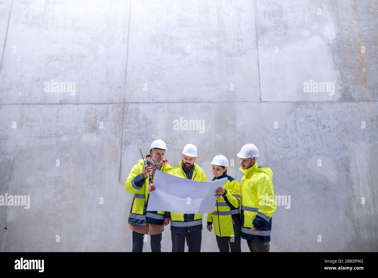 Un gruppo di ingegneri che si trova contro una parete in cemento nel cantiere. Foto Stock