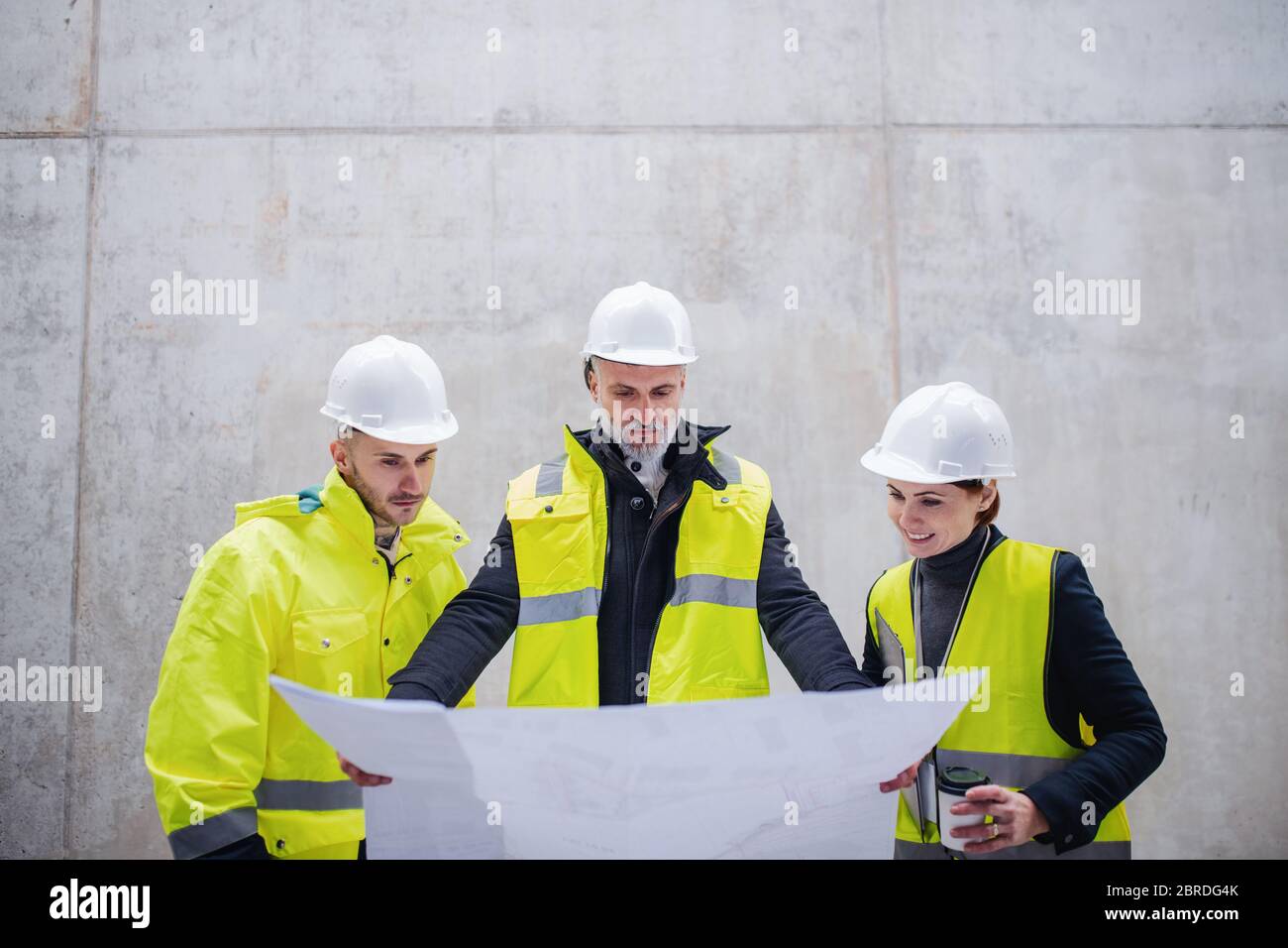 Un gruppo di ingegneri che si trova contro una parete in cemento nel cantiere. Foto Stock