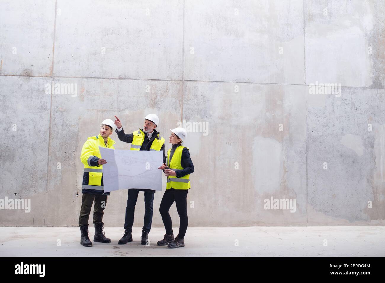 Un gruppo di ingegneri che si trova contro una parete in cemento nel cantiere. Foto Stock