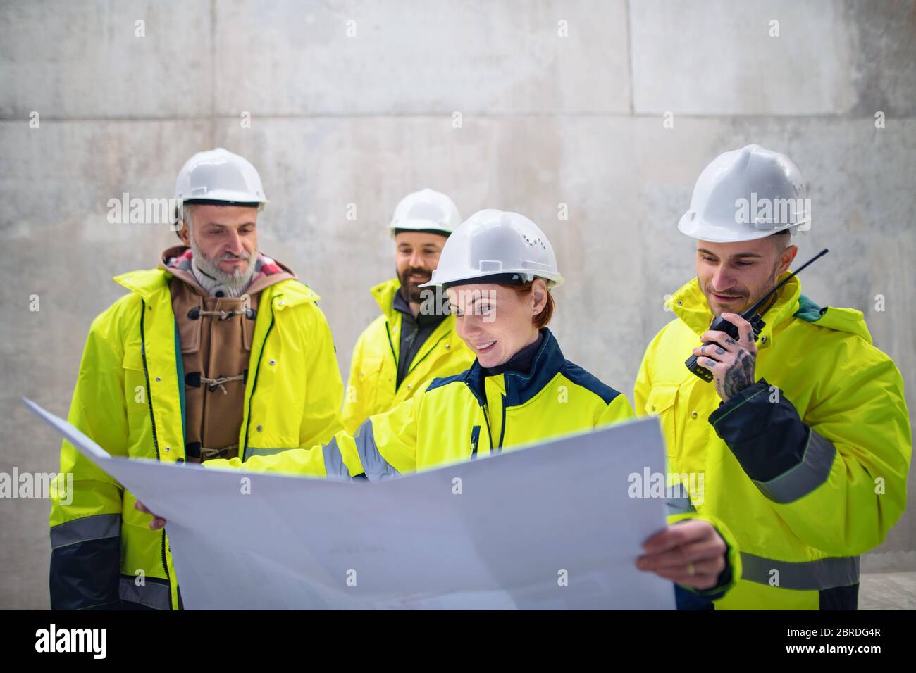 Un gruppo di ingegneri che si trova contro una parete in cemento nel cantiere. Foto Stock