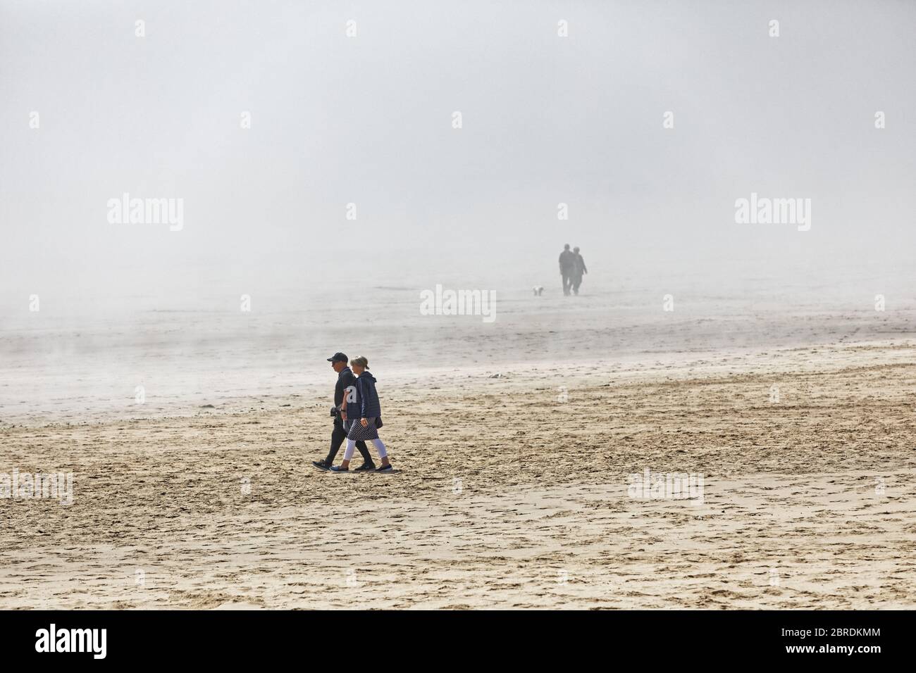 Le sagome di due persone camminano nella nebbia, mentre altre due persone camminano sulla sabbia nelle vicinanze della baia di Swansea Foto Stock