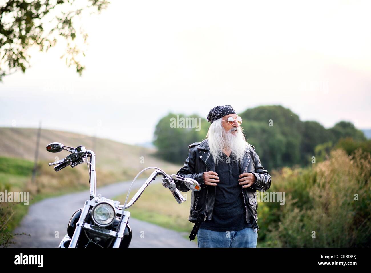 Uomo anziano con moto e occhiali da sole in campagna. Foto Stock