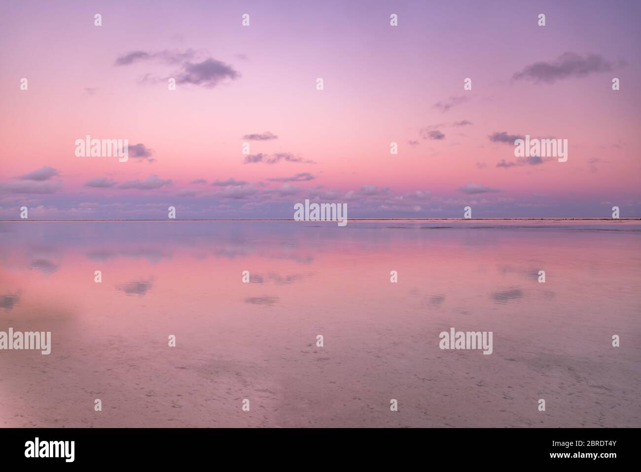 Calma e tranquillo tramonto zen in spiaggia con splendidi colori rosa e rosso con riflessi sull'acqua. Mare tranquillo e orizzonte Foto Stock