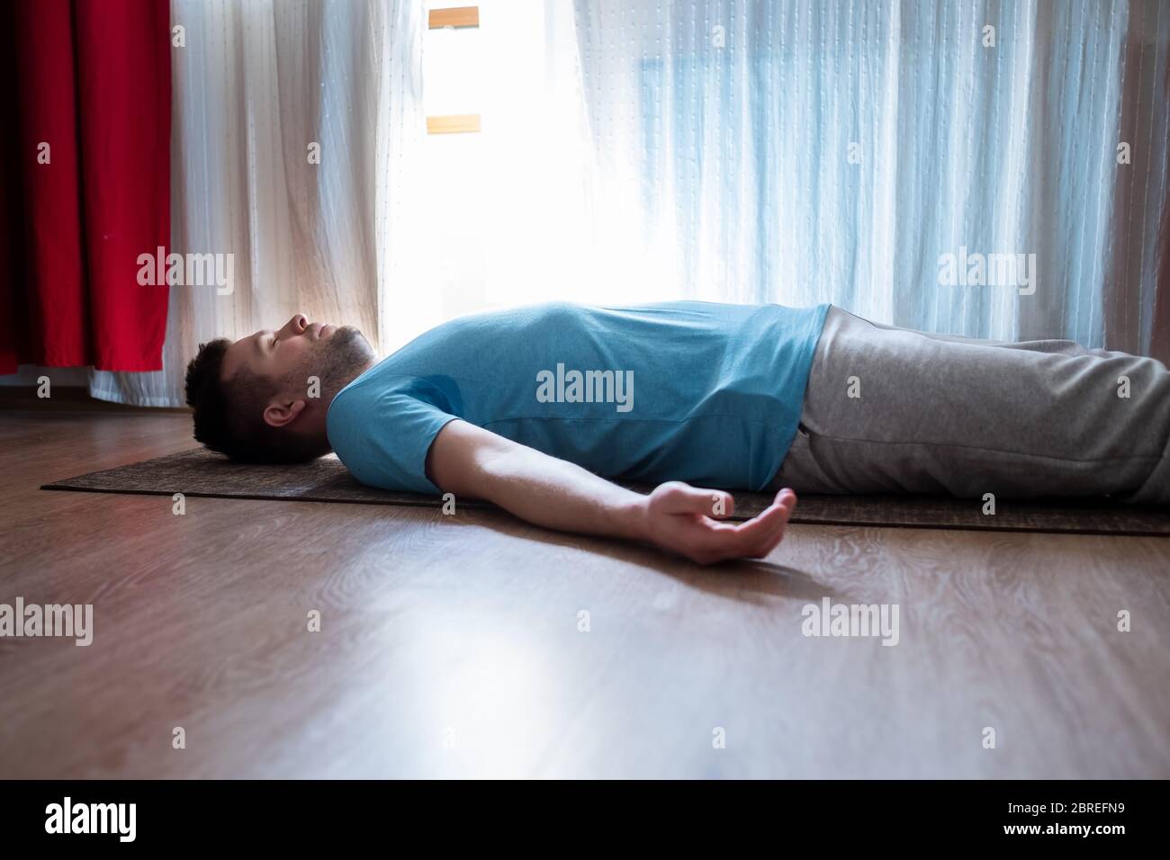 Il giovane meditating su un pavimento e sdraiato in Shavasana posa al suo soggiorno. Foto Stock