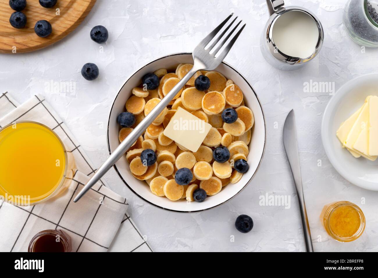 Minuscoli cereali con pancake. Colazione fatta in casa con mirtilli, marmellata e succo su sfondo grigio Foto Stock