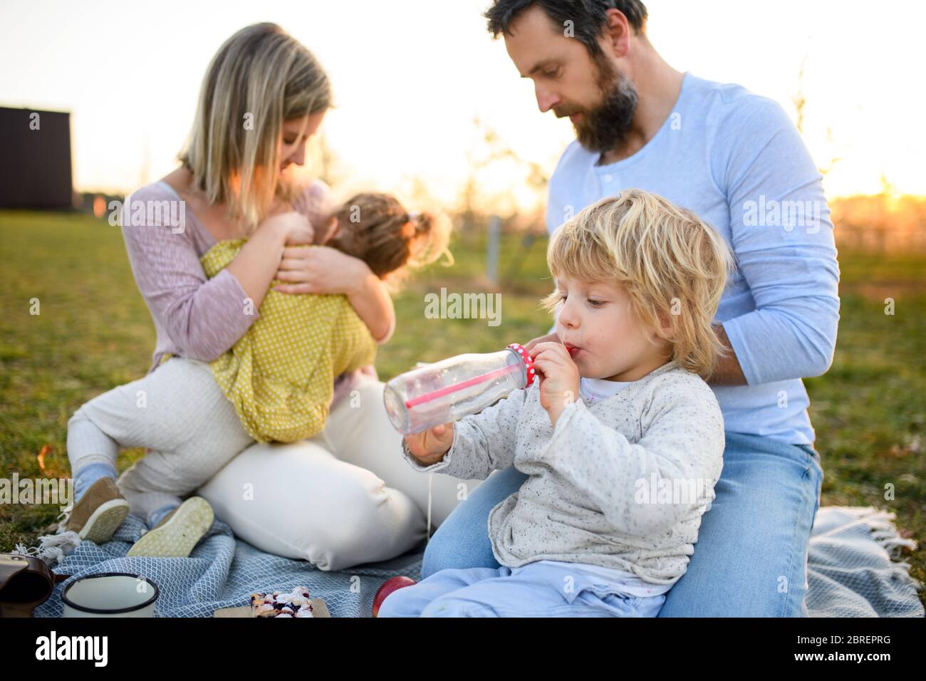 Famiglia con due bambini piccoli che hanno picnic all'aperto nella natura primaverile al tramonto. Foto Stock