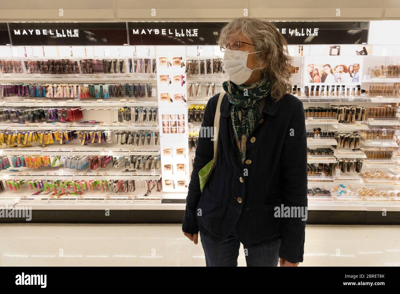 Una donna che indossa una maschera protettiva si trova di fronte a un'esposizione di cosmetici in un negozio al dettaglio Foto Stock