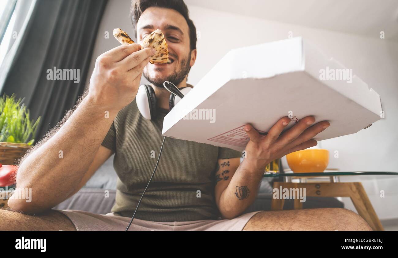 Giovane uomo che mangia pizza a casa - ragazzo felice che mangia mentre gioca a videogiochi in salotto - concetto di intrattenimento per i giovani e i cibi Foto Stock