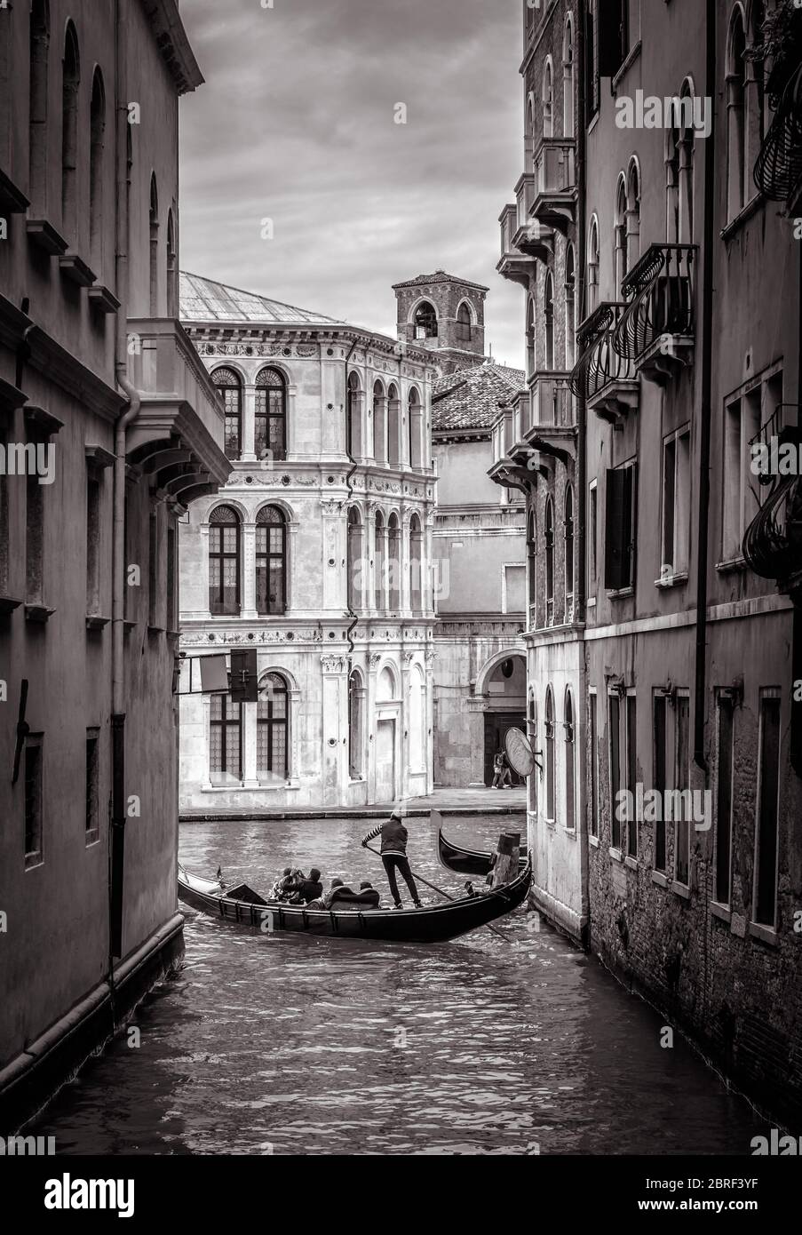 Venezia in bianco e nero, Italia. Vecchia strada stretta con gondola solita in lontananza. Romantica gita in acqua attraverso i canali vintage di Venezia. Concetto di tr Foto Stock