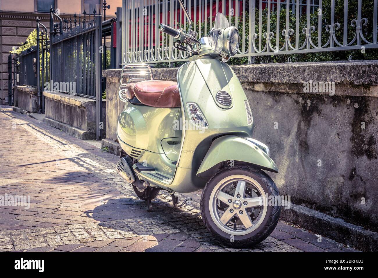 Scooter parcheggiato su una vecchia strada. Scooter o moto è uno dei mezzi di trasporto più popolari in Europa. Foto in stile vintage. Scena cittadina con verde retro Foto Stock