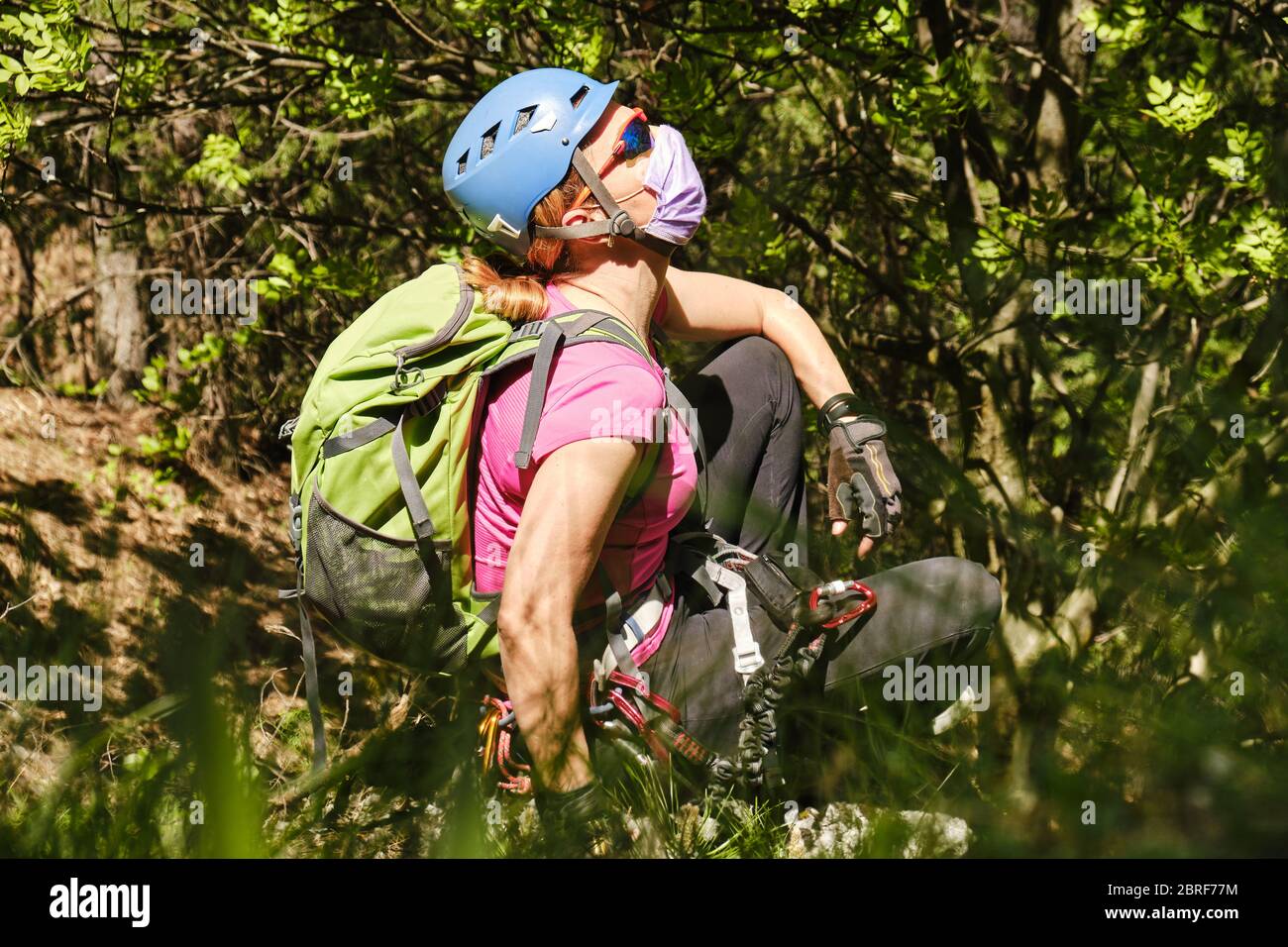 Donna alpinista con casco, zaino e maschera medica, gode l'aria fresca natura in una foresta. Concetto di Coronavirus (Covid-19) restrizioni bei Foto Stock