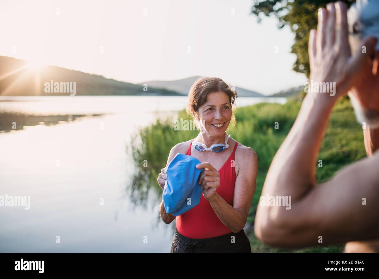 Coppia senior in costume da bagno in piedi vicino al lago all'aperto prima di nuotare. Foto Stock