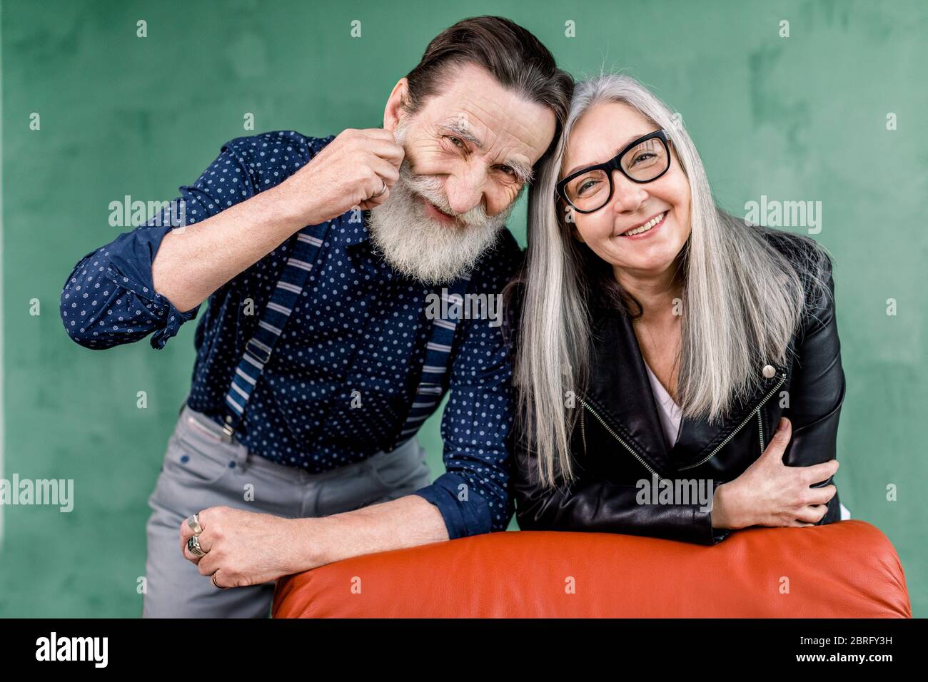 Coppia anziana. Allegra bella coppia anziana sorridente mentre è di grande umore, appoggiata su una sedia rossa morbida e toccando le fronte. Ritratto di romantico Foto Stock