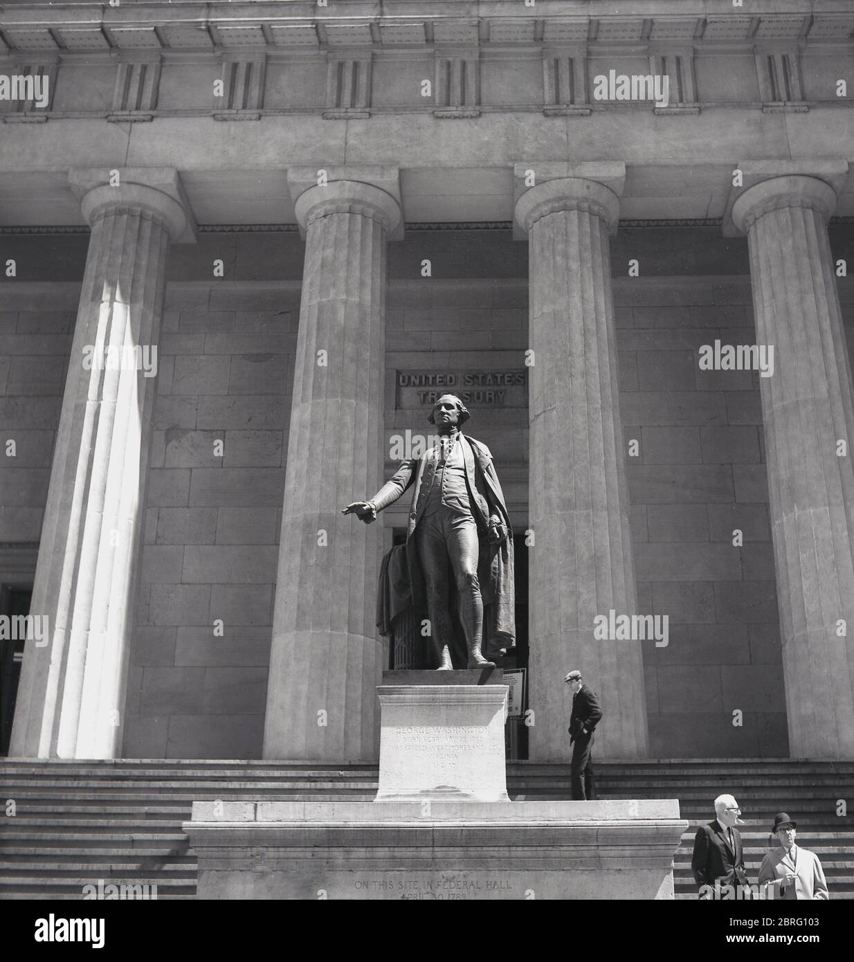 Anni '50, storico, vista esterna della Federal Hall, un grande edificio a colonne a Manhattan, New York, Stati Uniti. Inaugurato nel 1842 per la Custom House degli Stati Uniti per il Porto di New York e costruito in stile architettonico greco revival, è servito come un edificio sub-tesoro e sostituito un edificio precedente ufficialmente noto come 'Federal Hall'. La statua di bronzo di George Washington di John Qunicy Adams Ward sui gradini dell'edificio commemora il luogo in cui è stato giurato come primo presidente della nazione. Foto Stock
