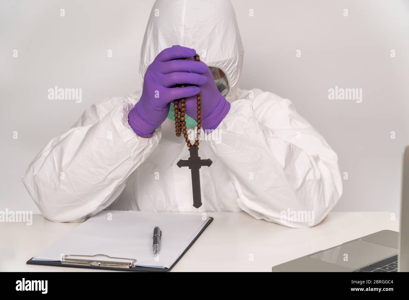I medici in tute e maschere protettive tengono una croce e pregano per la speranza di trattare e prevenire l'infezione, il concetto di diffusione Coro Foto Stock