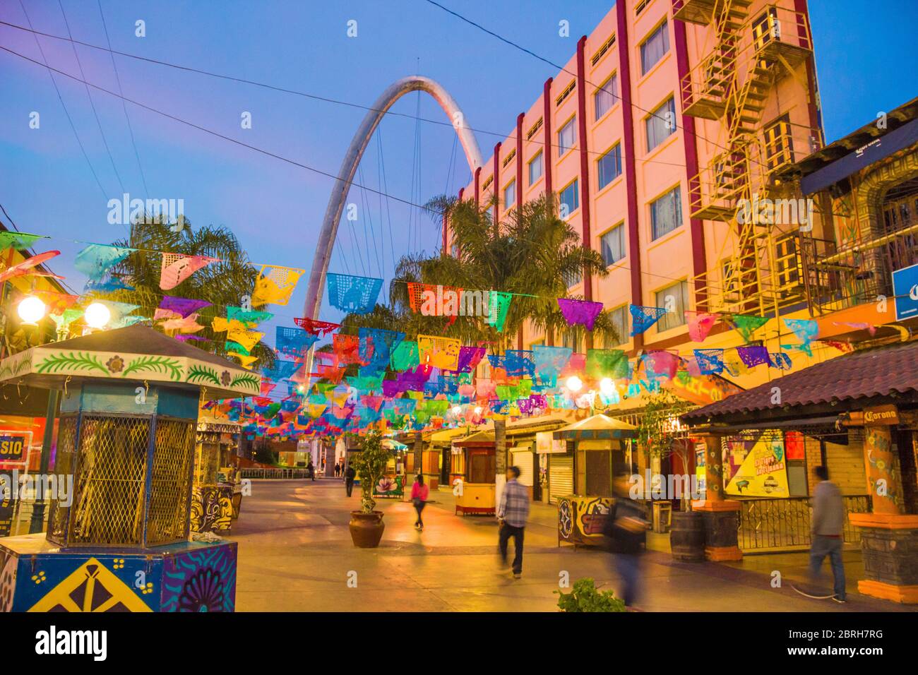 Santiago Arguello strada pedonale per lo shopping e bar con bandiere di festival sopra e arco millenario (El arco y reloj monumentale). Tijuana, Messico Foto Stock