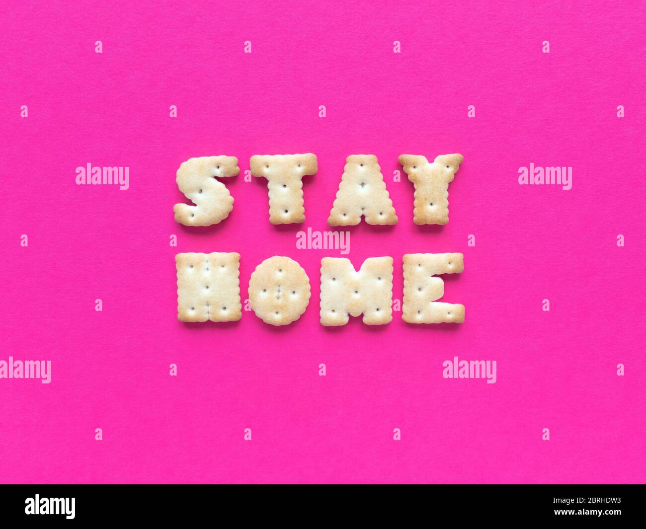 Rimani a casa. Citazione di quarantena da cracker su sfondo rosa. Semplice disposizione piatta con texture pastello. Foto di scorta. Foto Stock