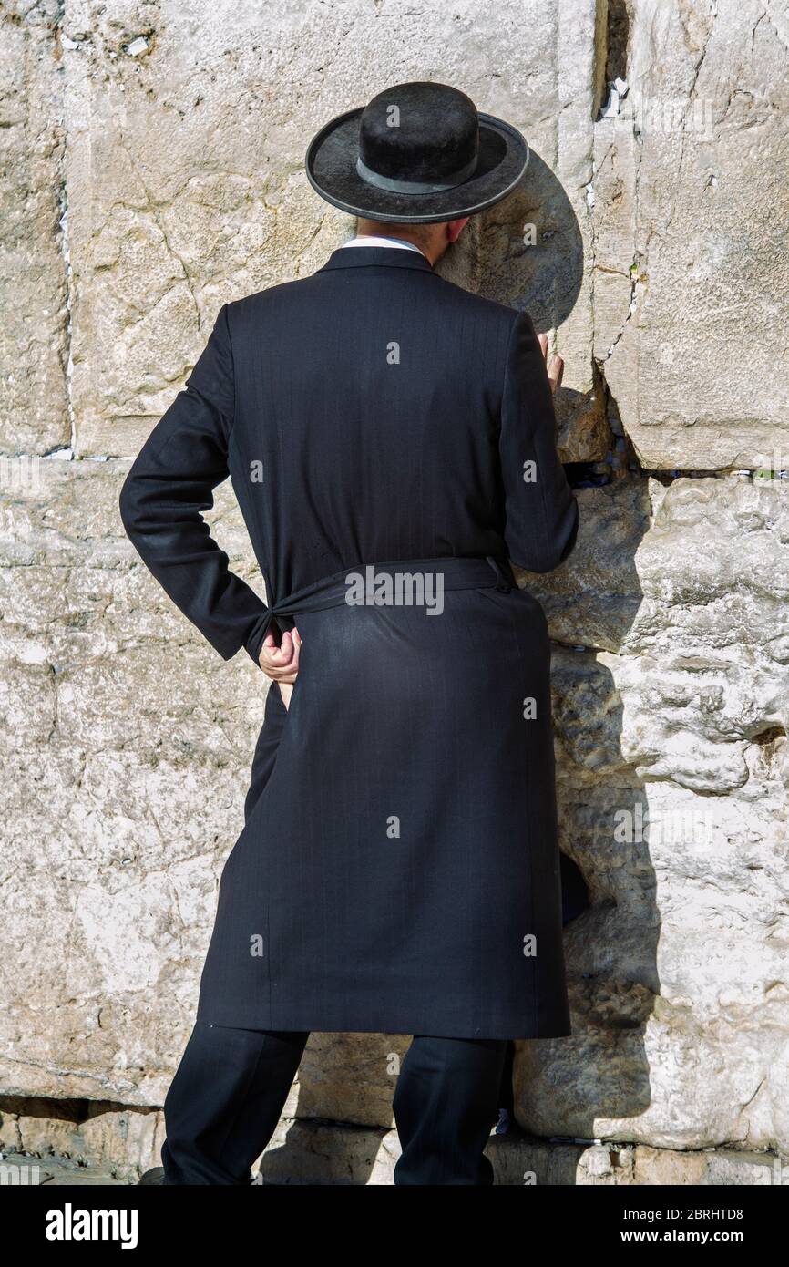 Un uomo religioso, vestito di nero, che prega al 'Wailing Wall' o al Muro  Occidentale nella Città Vecchia di Gerusalemme. Pietra della Fondazione,  più sacra al giudaismo, dietro il muro Foto stock -