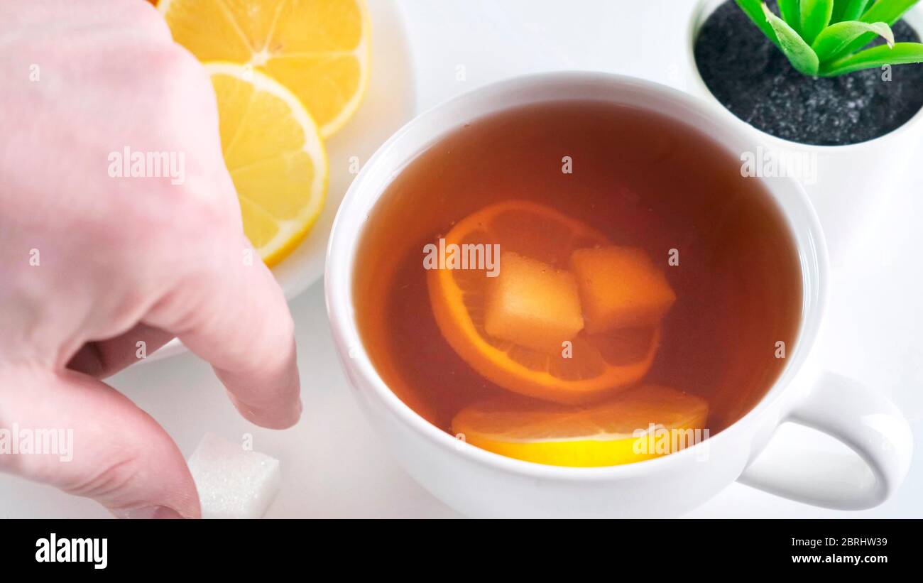 Aggiungere lo zucchero alla tazza di tè del whute sul tavolo della cucina. Primo piano. Foto Stock