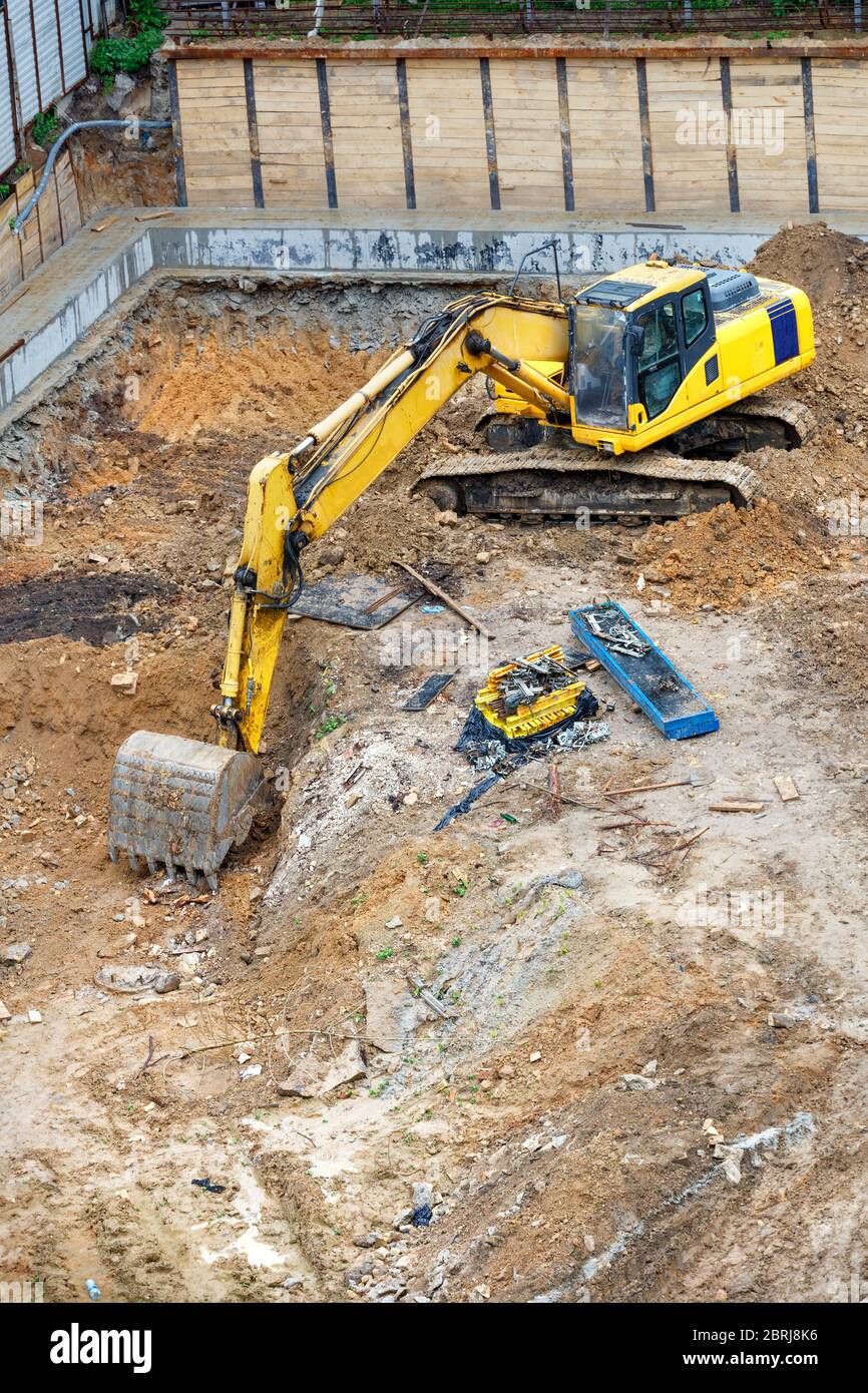 Un grande escavatore giallo scava una fossa di fondazione in un nuovo cantiere, angolo di visione da un'altezza, immagine verticale, spazio di copia. Foto Stock