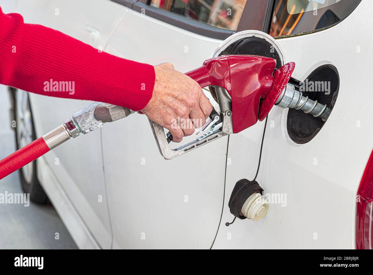 Primo piano orizzontale di una donna anziana che pompa benzina nella sua auto bianca. Foto Stock