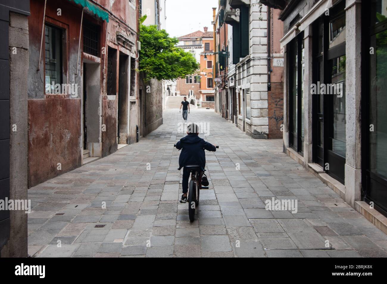 VENEZIA, ITALIA - MAGGIO: Un bambino corre in bicicletta nelle strade vuote il 18 maggio 2020 a Venezia, Italia. Ristoranti, bar, caffè, parrucchiere e altri negozi Foto Stock