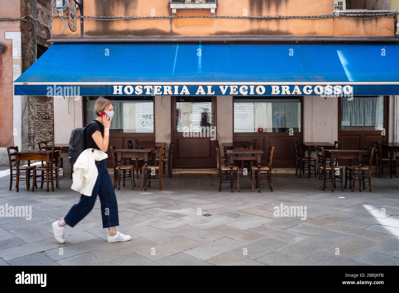 VENEZIA, ITALIA - MAGGIO: Una donna cammina di fronte ad un ristorante appena riaperto il 18 maggio 2020 a Venezia. Ristoranti, bar, caffè, parrucchiere e. Foto Stock