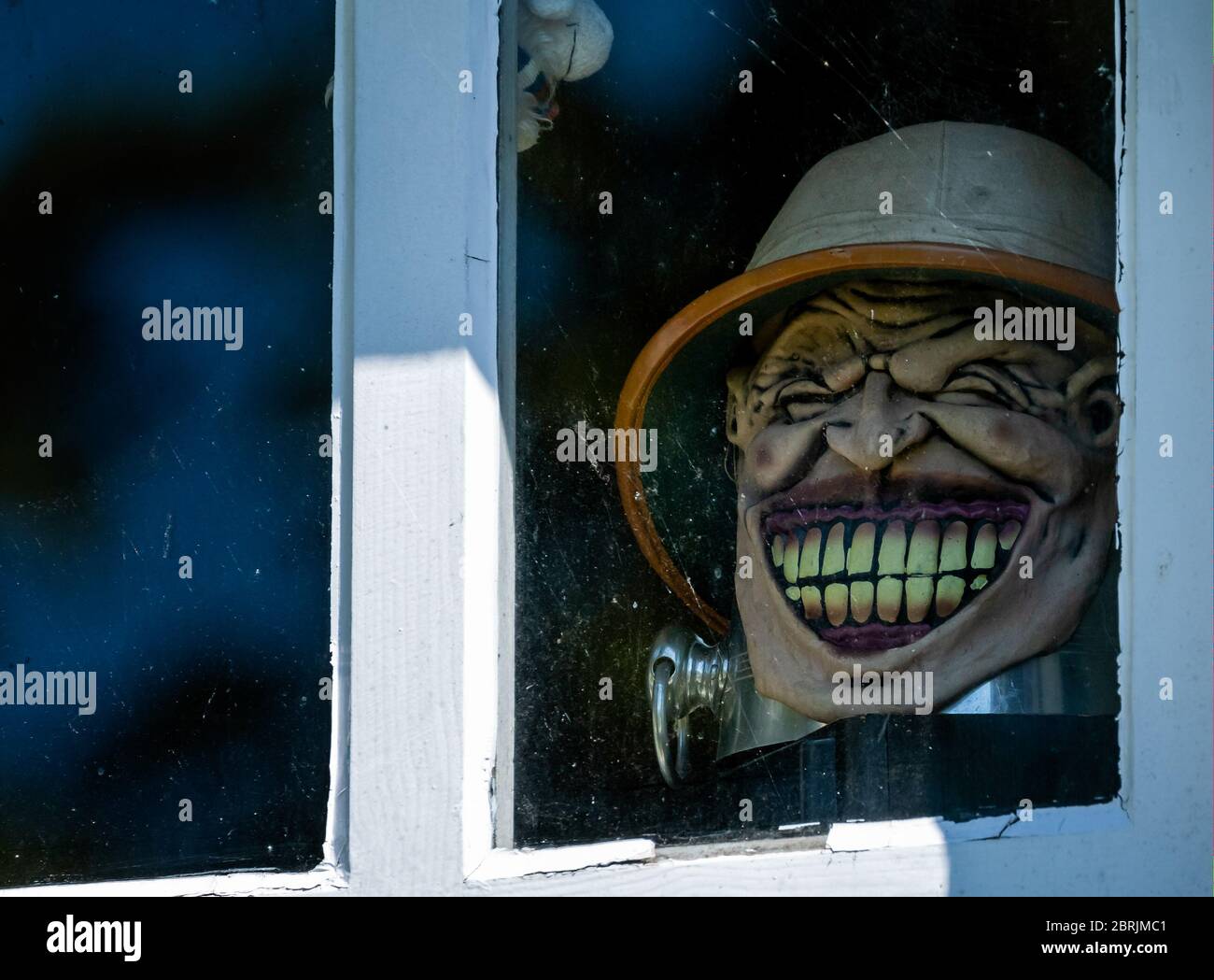 Spaventosa maschera di testa del cacciatore Safari con il sorriso malvagio che si apre attraverso la finestra Foto Stock