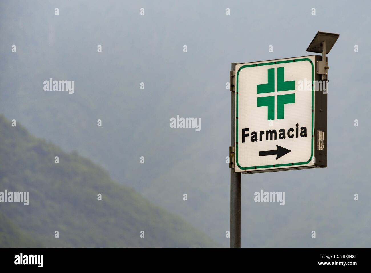 LAGO DI COMO, ITALIA - 2019 GIUGNO: Cartello che indica la strada per una Farmacia in una delle città che costeggiano il lago di Como, sulla sommità è presente un pannello solare per alimentarlo Foto Stock