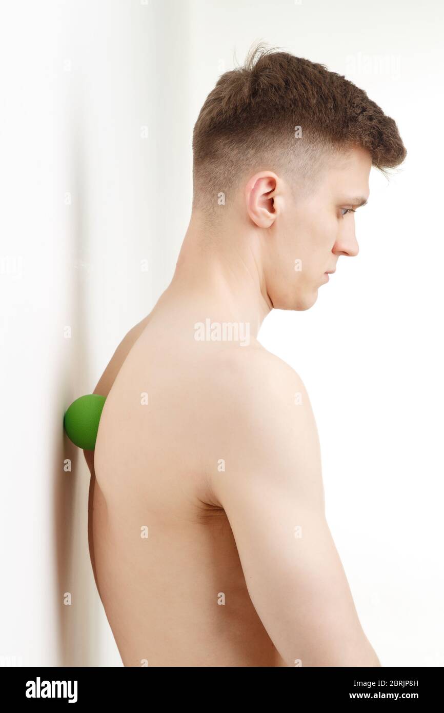 Bell'uomo mostra esercizi utilizzando la parete e la mini palla fitness per un massaggio di rilascio miofasciale dei punti di innesco. Massaggio del muscolo della colonna vertebrale Foto Stock